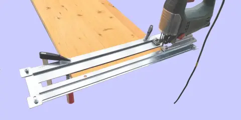 Une scie sauteuse sur un guide pour découper une planche de bois.