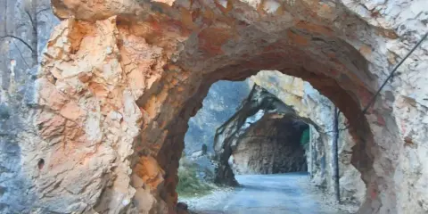 Un túnel natural en la ruta del silencio Teruel, con paredes de roca rojiza y un camino que se adentra en la montaña.