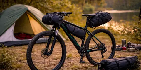 Rower gotowy do bikepacking gravel. Namiot i sprzęt kempingowy czekają nad jeziorem.