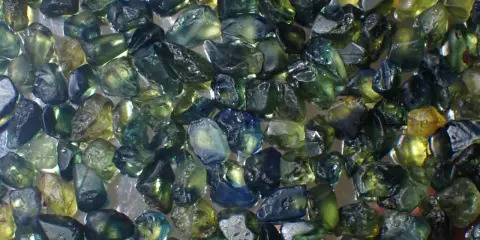 Un mucchio di zaffiri grezzi australiani, con sfumature verdi, blu e gialle. Il loro valore è legato alla rarità e alla bellezza di queste gemme naturali.