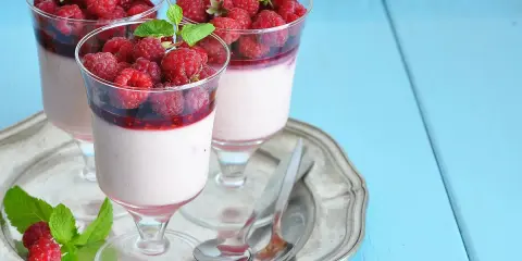 Trois panna cotta onctueuses, garnies de framboises fraîches et d'un coulis de framboise, sur un plateau argenté.