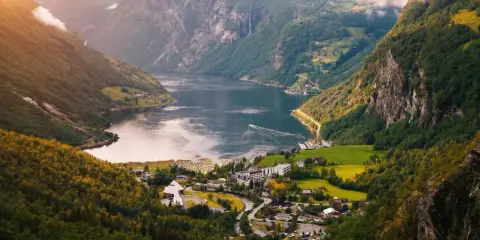 Majestätisk natur i Norge med en djup fjord, branta berg täckta av grönska och ett litet samhälle vid vattnet.