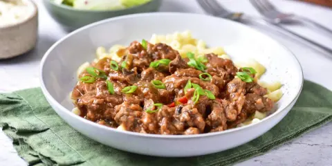 Pyszny strogonow z wieprzowiny z pieczarkami i ogórkiem kiszonym, podany z makaronem. Idealny przepis na obiad.
