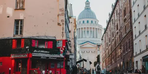 Urokliwa uliczka w paryskiej dzielnicy łacińskiej z czerwonym bistro i majestatycznym Panteonem w tle.