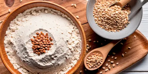 Farine au froment ou au blé noir dans un bol en bois, garnie d'amandes. Des graines sont dans des cuillères et sur un plateau.