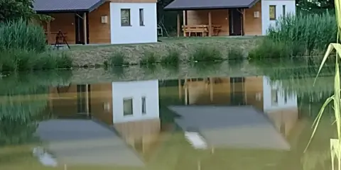 Urokliwe łowisko z domkami letniskowymi, których odbicia tańczą na spokojnej tafli wody.