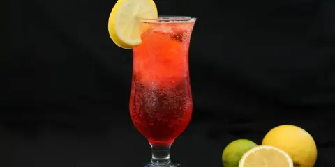 Orzeźwiający drink z granatem, ozdobiony plasterkiem cytryny. Obok leżą świeże owoce: cytryna i limonka.