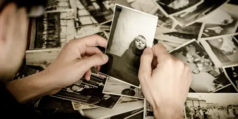 Ręce przeglądają stare fotografie, tworząc osobistą archiwizację zdjęć. Widać portret dziecka i grupowe ujęcia.