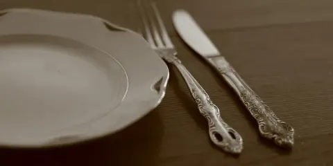 Une assiette blanche et des couverts en métal argenté, prêts pour un repas. L'art de nettoyer des couverts en métal argenté pour qu'ils brillent.
