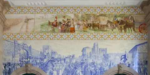 Azulejos de Oporto narran la historia: un tren antiguo, gente vestida de época y una procesión militar en azul y blanco.