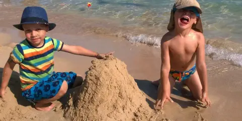 Bambini felici in vacanza in Puglia, costruiscono un castello di sabbia sulla spiaggia con il mare cristallino sullo sfondo.