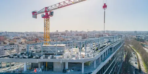 Grue de chantier sur un bâtiment en construction rapide, avec une ville en arrière-plan.