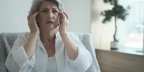 Donna anziana con mani sulle tempie, espressione preoccupata, forse un momento di **perdita di memoria improvvisa**.