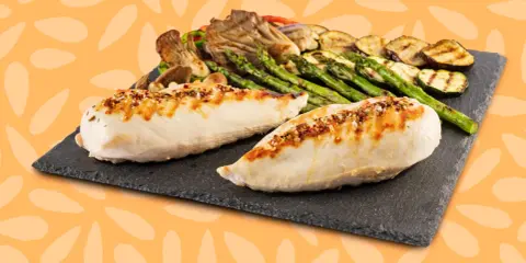 Dos jugosas pechugas de pollo a la parrilla, sazonadas con especias, acompañadas de espárragos, calabacín y champiñones.