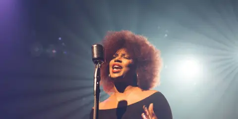 Kobieta z burzą afro włosów śpiewa do mikrofonu, jej głos jest niczym unchained melody, wolny i pełen emocji.