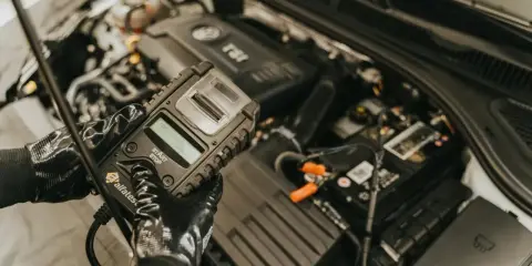 Mechanik w rękawiczkach trzyma tester akumulatora, który może zawierać czujnik Halla, sprawdzając stan pojazdu.