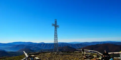 Metalowy krzyż na szczycie, ławki i kamieniste podłoże. W oddali widać pasma górskie. To jedne z wielu **Bieszczady atrakcje**.