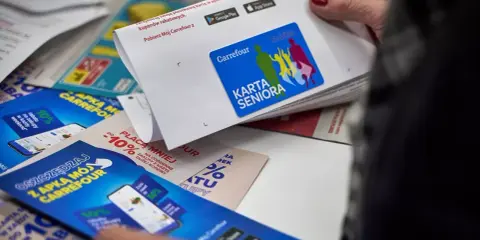 Karta Seniora Carrefour daje zniżki i rabaty. Na zdjęciu widać ulotki i kartę z logo Carrefour.