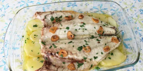Lubina a la espalda horneada con patatas, ajo y perejil en una fuente de cristal.