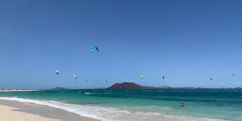Kitesurfer tanzen über das türkisfarbene Wasser am Flag Beach Corralejo. Ein einsamer Schwimmer genießt die Sonne.