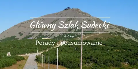 Kamienista ścieżka prowadzi na szczyt góry, gdzie widać budynek. Nad krajobrazem widnieje napis "Główny Szlak Sudecki".