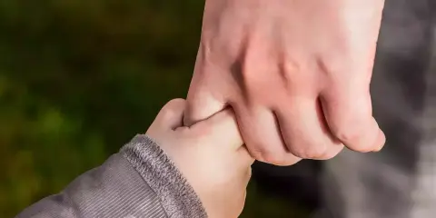 Dłoń dorosłego, opiekuna prawnego, mocno trzyma dłoń dziecka.
