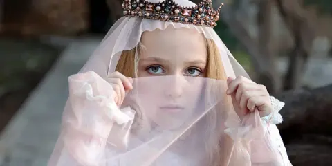 Ein Mädchen mit Krone und Schleier, wie eine Prinzessin aus Herr der Ringe Namen weiblich, blickt geheimnisvoll hervor.