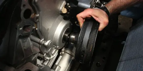 Mano retirando la polea del cigüeñal rota de un motor.