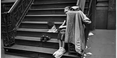 Una persona seduta sulle scale, con scarpe e cappello accanto. Un'immagine che evoca le cartier bresson foto famose, catturando un momento di vita urbana.