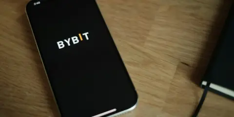 Smartfon z logo Bybit na ekranie, obok notatnik. Analiza bybit prowizje na urządzeniu mobilnym.