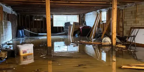 Un **garage inondé** avec de l'eau boueuse recouvrant le sol, des débris flottants et des matériaux de construction endommagés.
