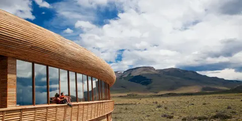 Coppia seduta su una terrazza di **edifici in legno famosi**, con vista su un paesaggio montano e cielo nuvoloso.