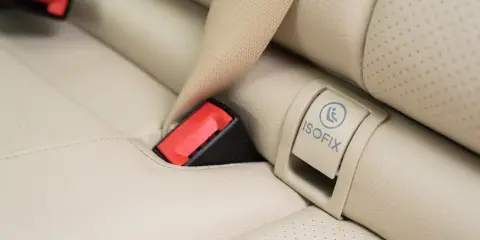 Zapięcie pasa bezpieczeństwa i oznaczenie ISOFIX na jasnej, skórzanej kanapie samochodowej. Czy baza isofix pasuje do każdego fotelika?