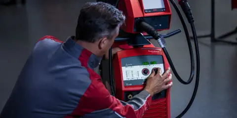 Operatore regola i parametri di saldatura su una macchina Fronius, ottimizzando l'apporto termico per un lavoro preciso.