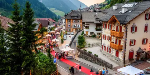 Festa a Santa Cristina Val Gardena con gente, bancarelle e un tappeto rosso.