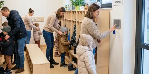 Rodzice odbierają dzieci z przedszkola. W szatni panuje ruch, dzieci ubierają się do wyjścia.