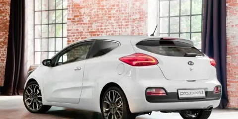 Biały Kia pro_ceed 1.6 CRDi z eleganckimi felgami stoi w stylowym wnętrzu z ceglaną ścianą i dużymi oknami.