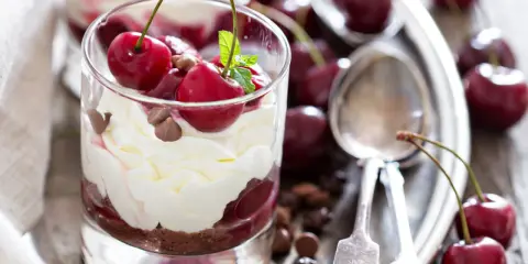 Delicioso postre con capas de crema batida, bizcocho de chocolate y cerezas frescas, coronado con más cerezas y trocitos de chocolate.