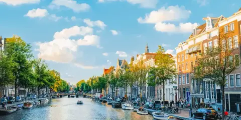 Widok na kanał w Amsterdamie, z łodziami, kamienicami i zielenią. Idealne miejsce, by poczuć, gdzie jest Amsterdam.