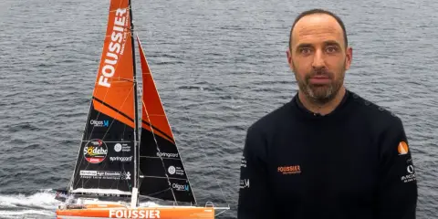 Sébastien Marsset, skipper du voilier Foussier, prêt pour la course. Le bateau orange et noir fend les vagues.