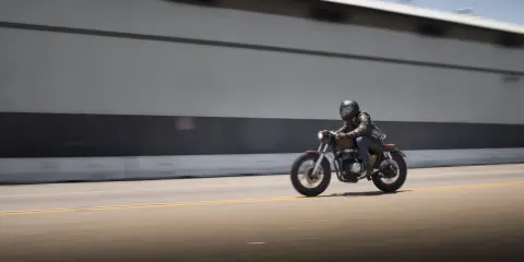 Motociclista con casco y chaqueta de cuero sobre una moto estilo cafe racer, en movimiento rápido por una carretera. El carmet a2 es su compañero de aventuras.