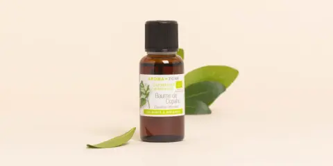Flacon de baume de copahu, une oléorésine naturelle aux vertus calmantes et apaisantes, entouré de feuilles vertes.
