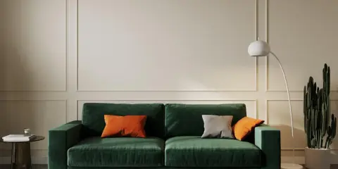 Elegancki salon w odcieniach butelkowej zieleni i beżu. Miękka sofa, nowoczesna lampa i kaktus tworzą przytulną atmosferę.