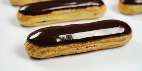 Plusieurs éclairs au chocolat brillants, avec un fondant pour éclair parfait, sont disposés sur fond blanc.