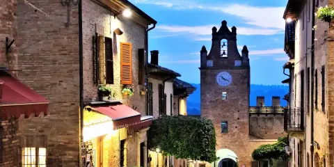 Borgo medievale illuminato al crepuscolo, con torre dell'orologio e vicoli suggestivi. Perfetto per scoprire cosa vedere vicino a Gradara.