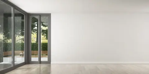 Un salon lumineux avec de grandes baies vitrées donnant sur un jardin verdoyant. Le parquet clair est parfait pour refaire le sol de la maison.