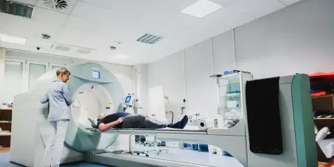 Pacjent leży na stole aparatu do tomografii komputerowej, nadzorowany przez technika.