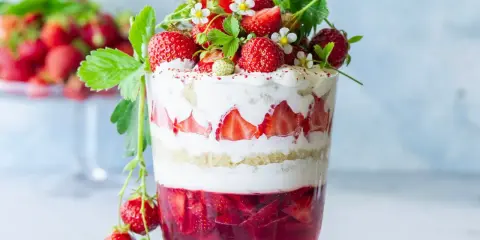 Verrine fraise fromage blanc, un délice estival en couches de génoise, crème et fruits rouges frais, décorée de fraises et de fleurs.