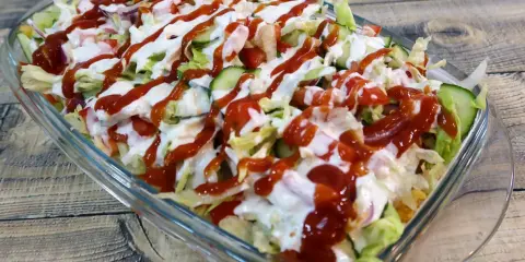 Kapsalon z kurczakiem, sałatą, pomidorami, ogórkiem i sosami w szklanej misce.
