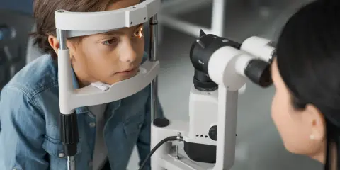 Chłopiec podczas badania wzroku. Okulista wykonuje biometrię oka, analizując jego strukturę.